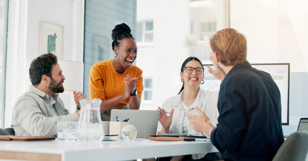 A marketing team of four professionals sits happily around a conference table to discuss brand awareness.