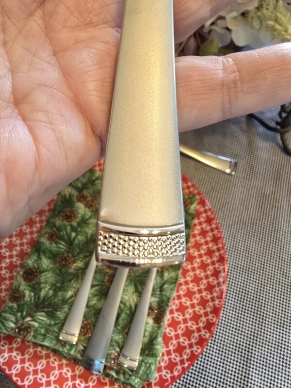 Close-up of a gold-toned lipstick case being held in a hand, showing the textured silver cap at the bottom.