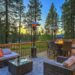 A cabin deck features a couch, several chairs, and a table with a fire. It sits next to a forest with tall trees.