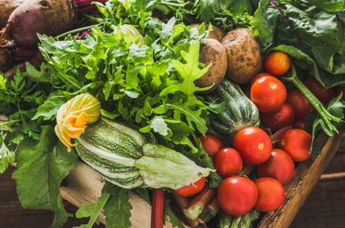 A wooden crate filled with fresh garden vegetables, including tomatoes, zucchini, leafy greens, and root crops.