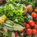 A wooden crate filled with fresh garden vegetables, including tomatoes, zucchini, leafy greens, and root crops.