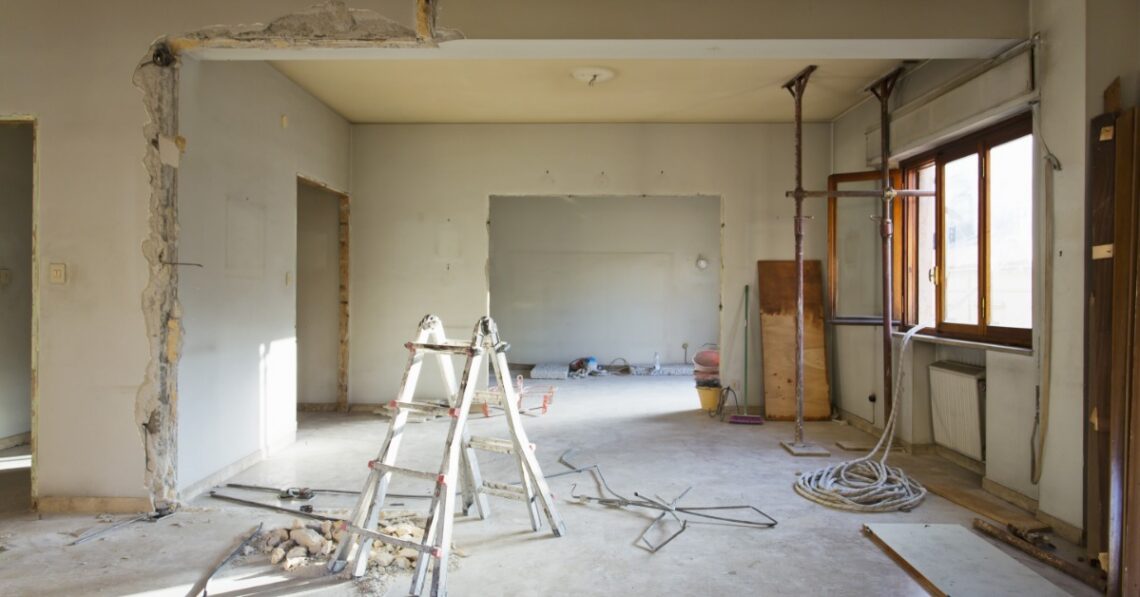 An unfinished home interior renovation with exposed wall openings, support posts, cables, and construction debris.