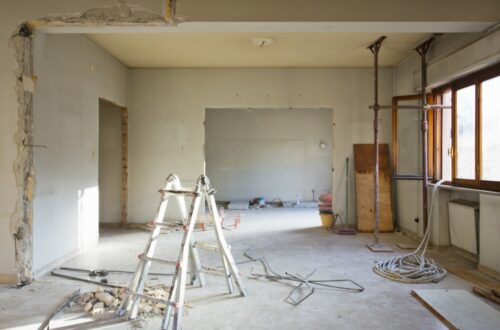 An unfinished home interior renovation with exposed wall openings, support posts, cables, and construction debris.