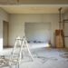 An unfinished home interior renovation with exposed wall openings, support posts, cables, and construction debris.