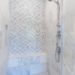 A walk-in shower covered in white and grey tile with a patterned back wall and a small concrete bench in the back.