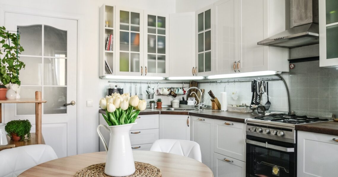 A small kitchen with white cabinets and clean appliances. There is a small table holding tulips in a vase.