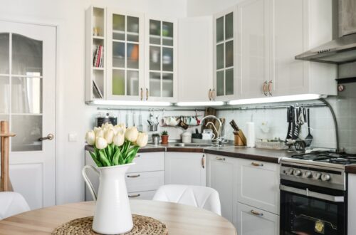 A small kitchen with white cabinets and clean appliances. There is a small table holding tulips in a vase.