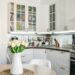 A small kitchen with white cabinets and clean appliances. There is a small table holding tulips in a vase.