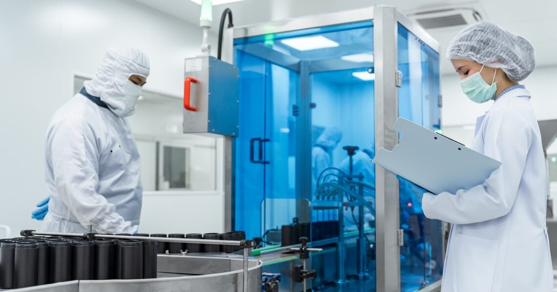 Two workers in a cleanroom overseeing large black medical device parts moving along a conveyor belt. Durable Medical Devices