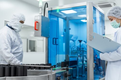 Two workers in a cleanroom overseeing large black medical device parts moving along a conveyor belt. Durable Medical Devices