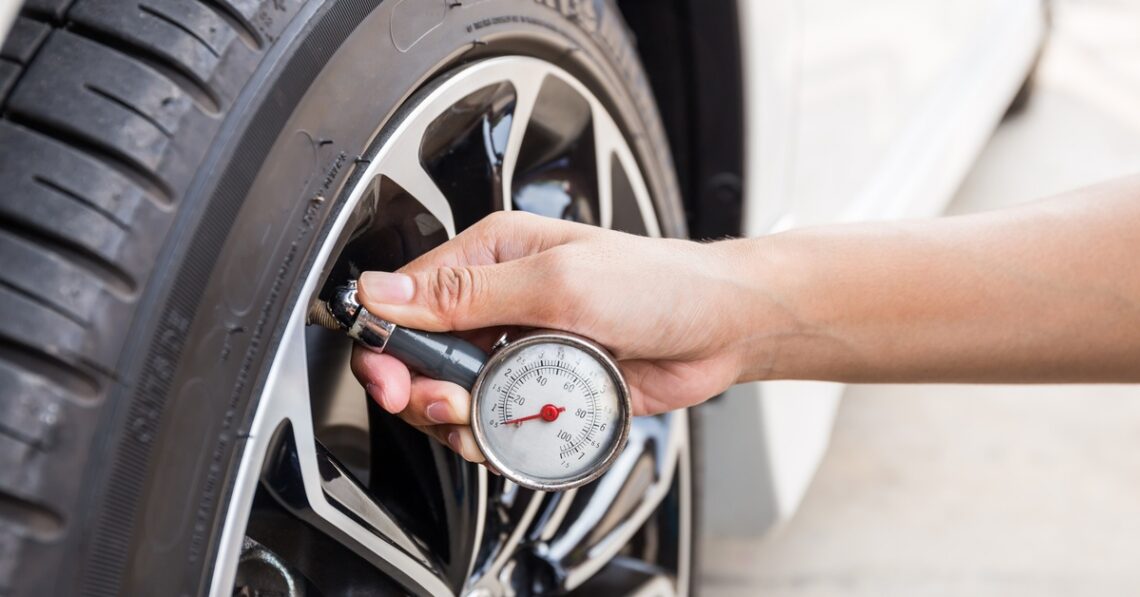 A person attaching a small air pressure gauge to the tire on a clean white car outside on a sunny day.