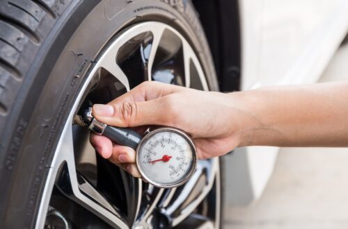 A person attaching a small air pressure gauge to the tire on a clean white car outside on a sunny day.