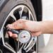 A person attaching a small air pressure gauge to the tire on a clean white car outside on a sunny day.